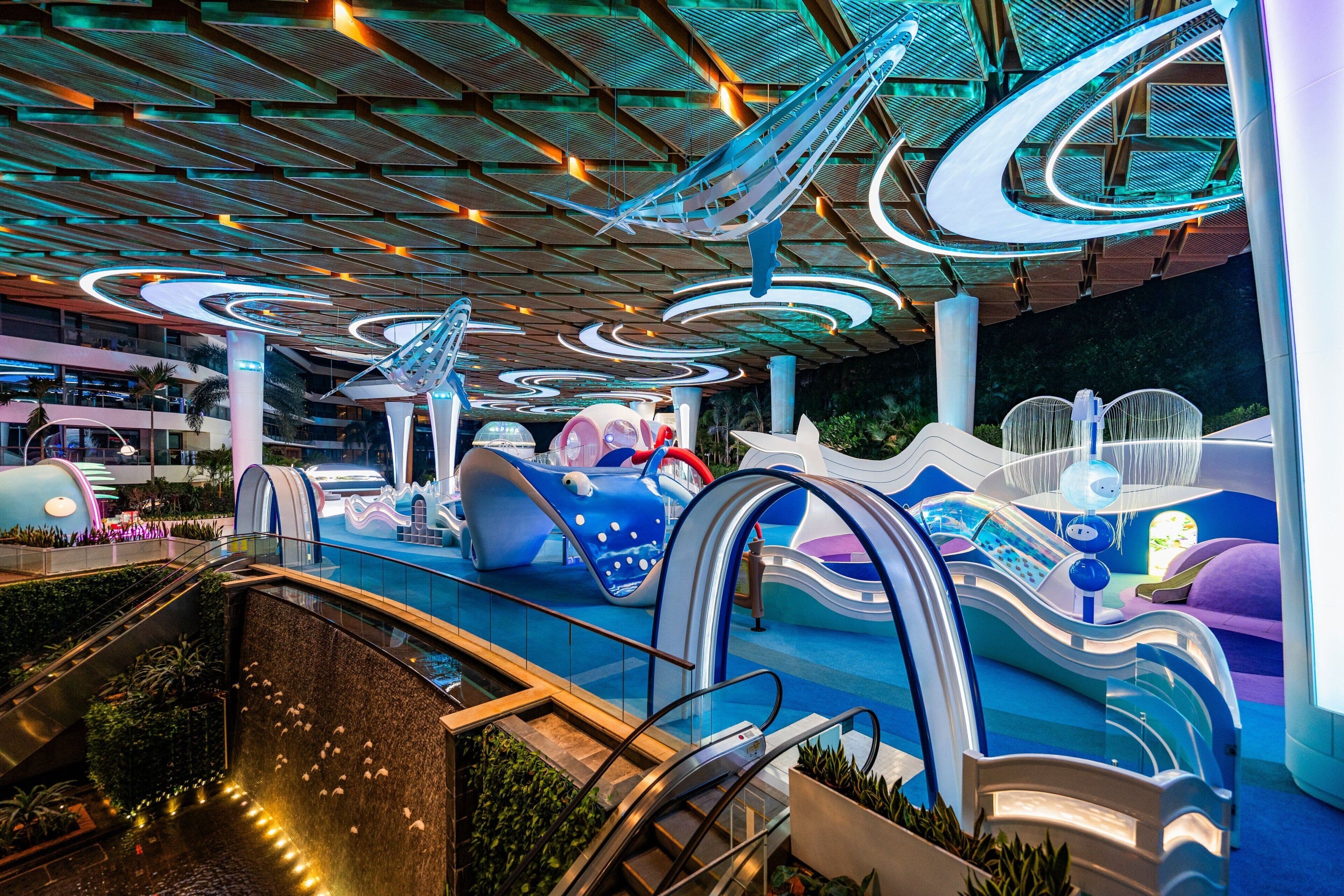 A modern indoor space with escalators, a pool area, and a children's play zone.