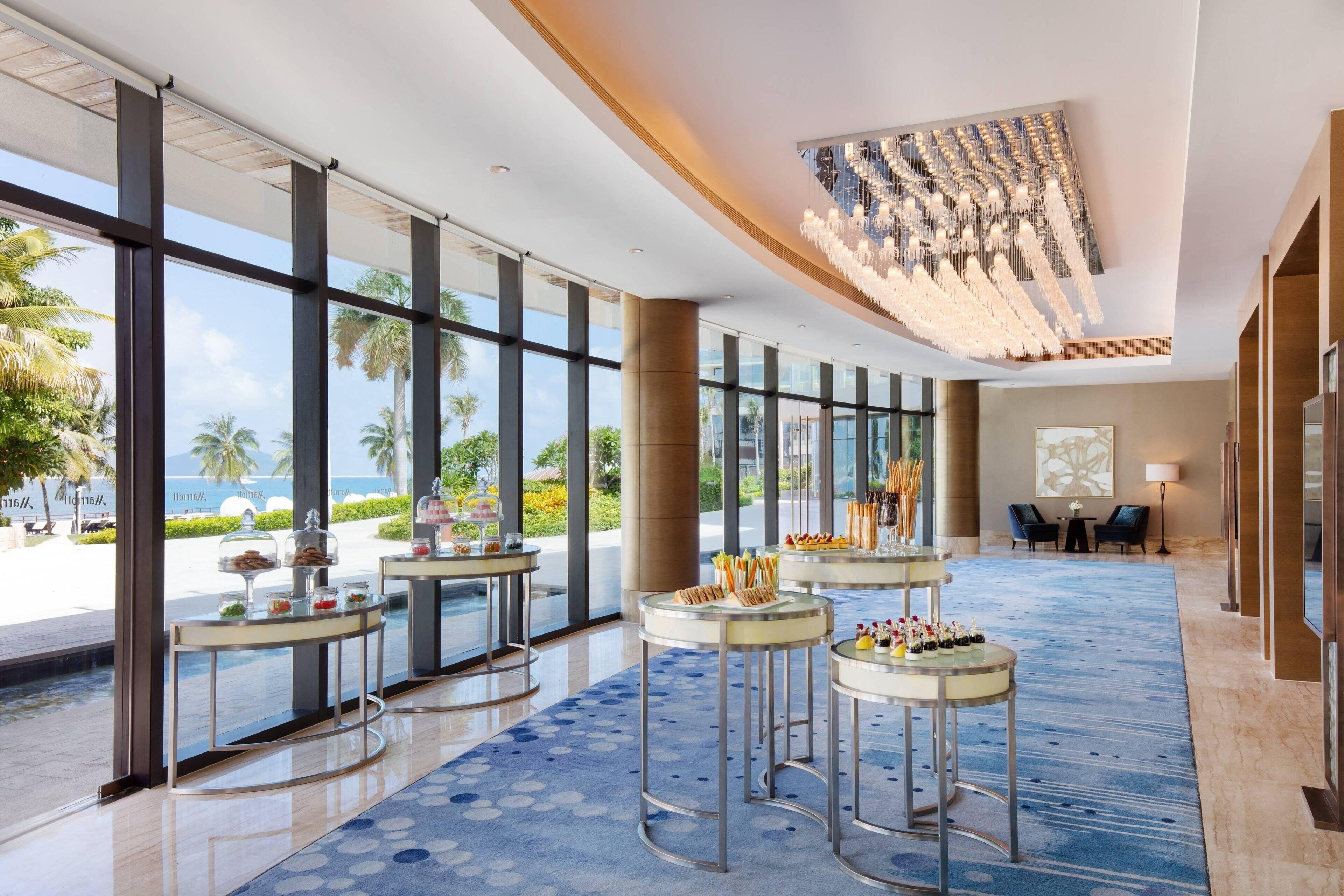 A spacious lobby with large windows, a blue patterned carpet, and several round tables with food displays.