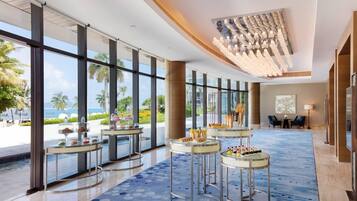 A spacious lobby with large windows, a blue patterned carpet, and several round tables with food displays.