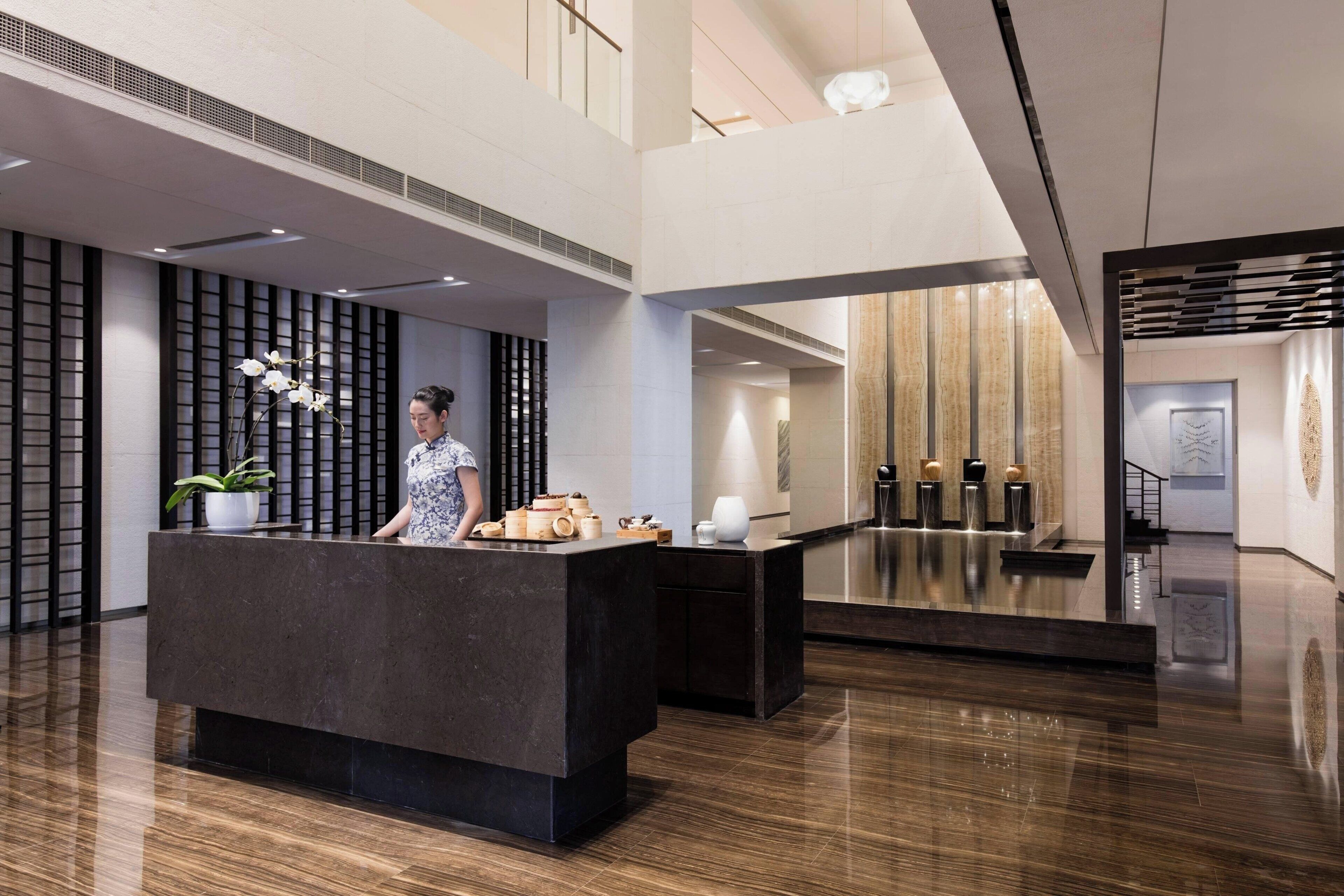 A modern reception area with a dark reception desk, a potted plant, and a decorative vase.