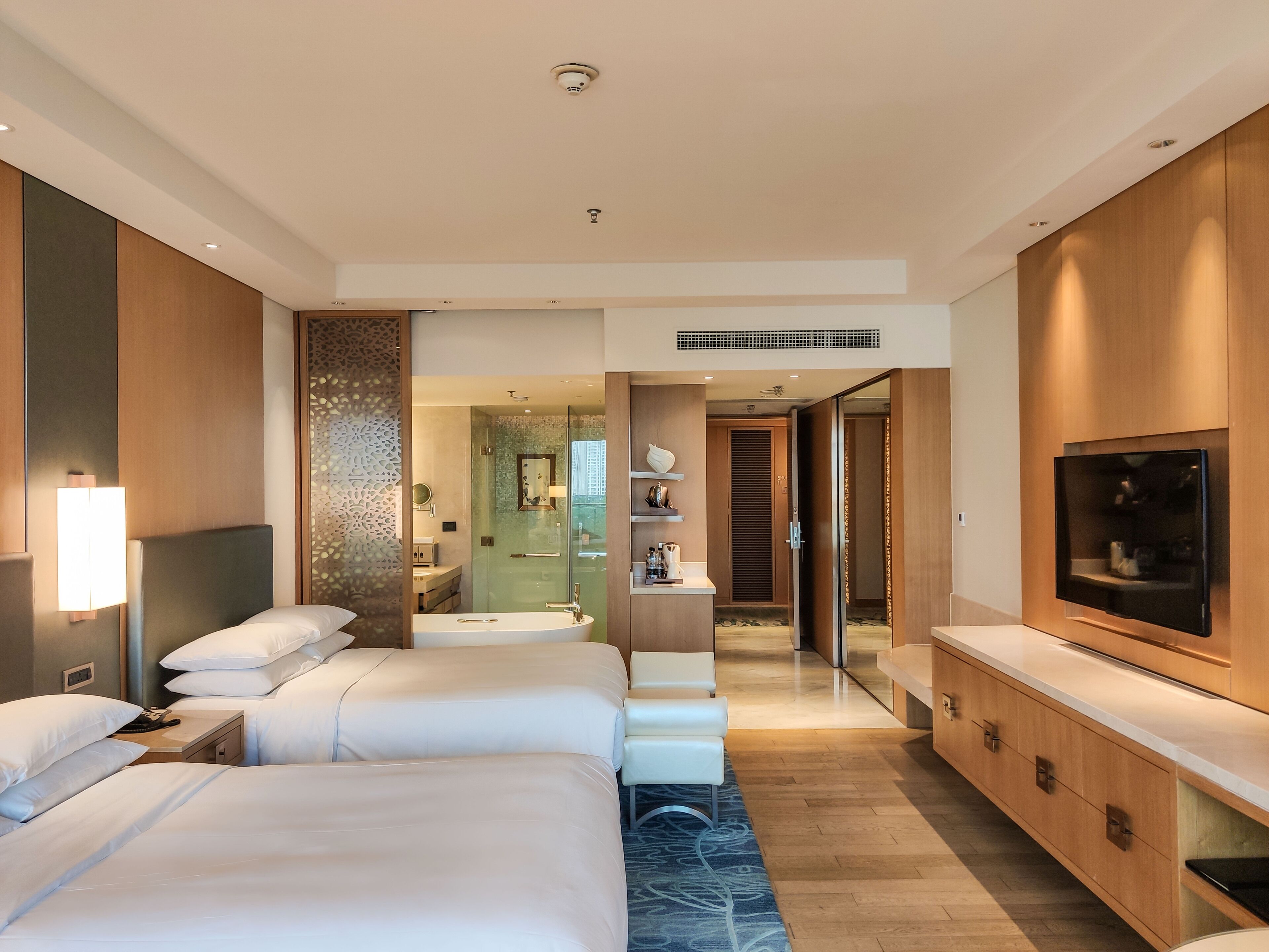 A hotel room with two beds, a TV, a minibar, and a bathroom visible through an open door.