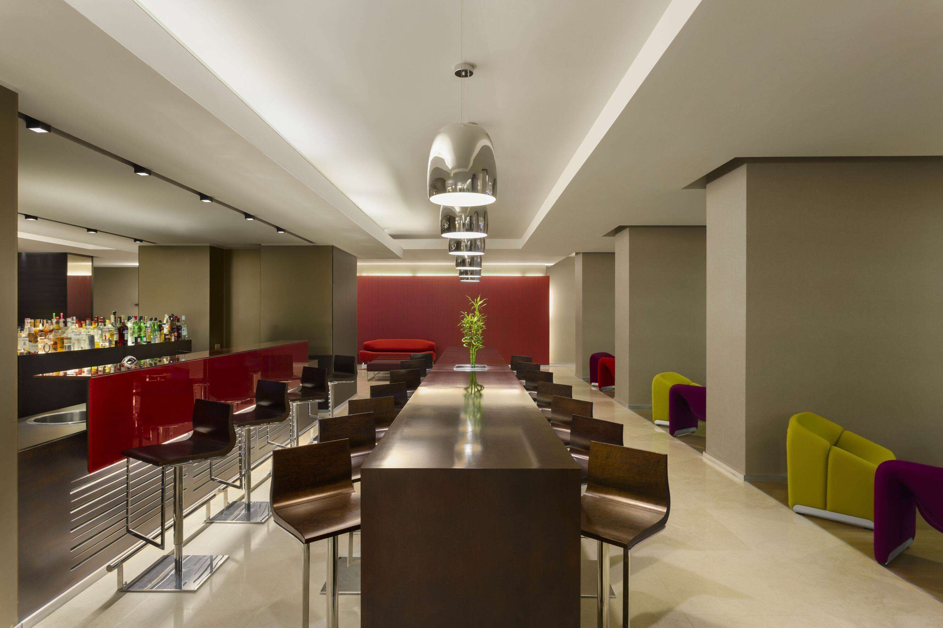 A modern bar area with a long counter, multiple bar stools, and a central table.