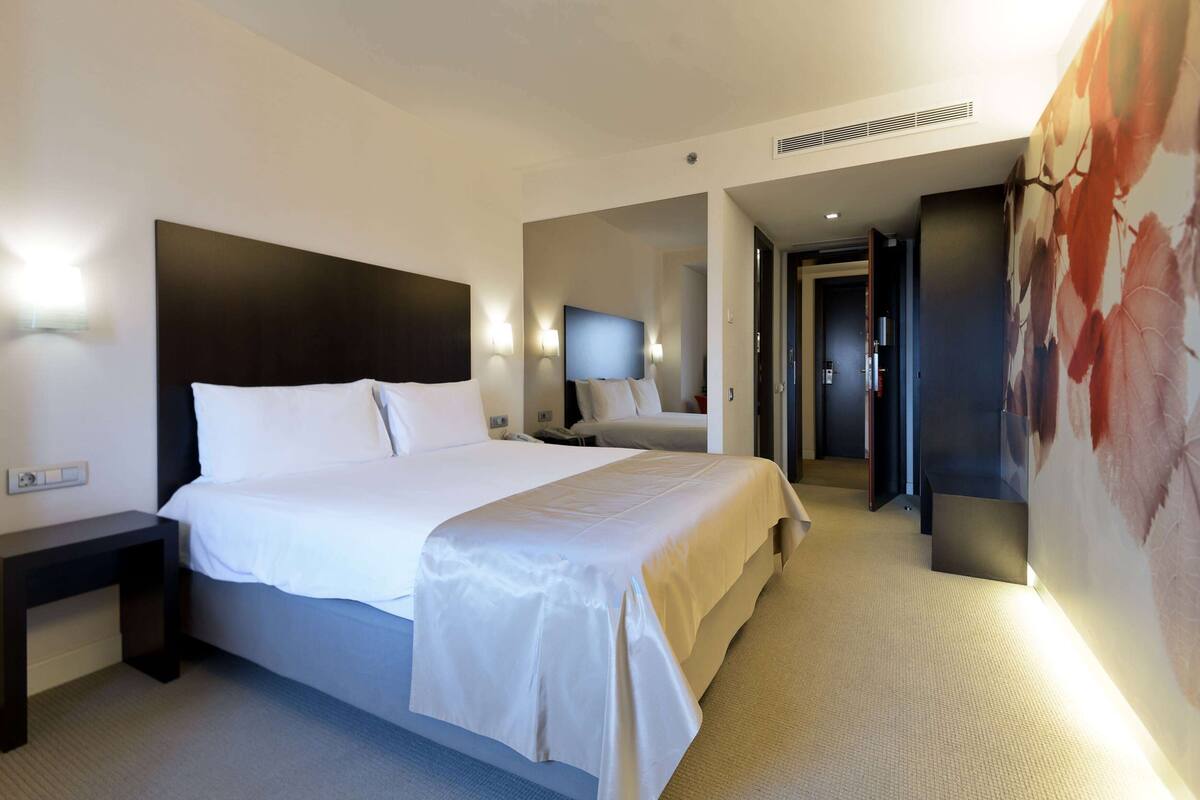 Ein Hotelzimmer mit einem großen Bett, einem Nachttisch, einem Flachbildfernseher und einem wandmontierten Spiegel.