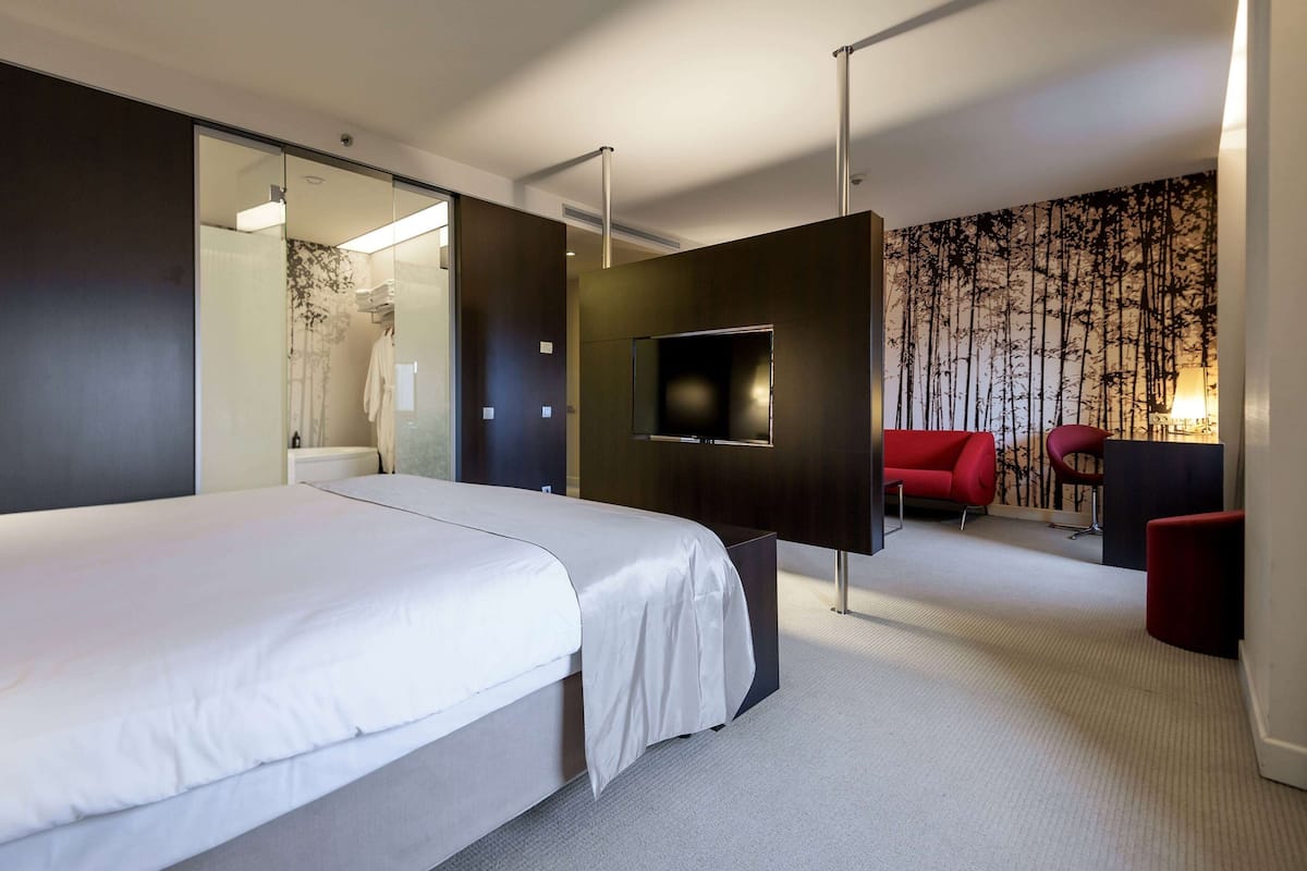Ein modernes Hotelzimmer mit einem großen Bett, einem Flachbildfernseher, einem roten Sessel und einem Schreibtisch.