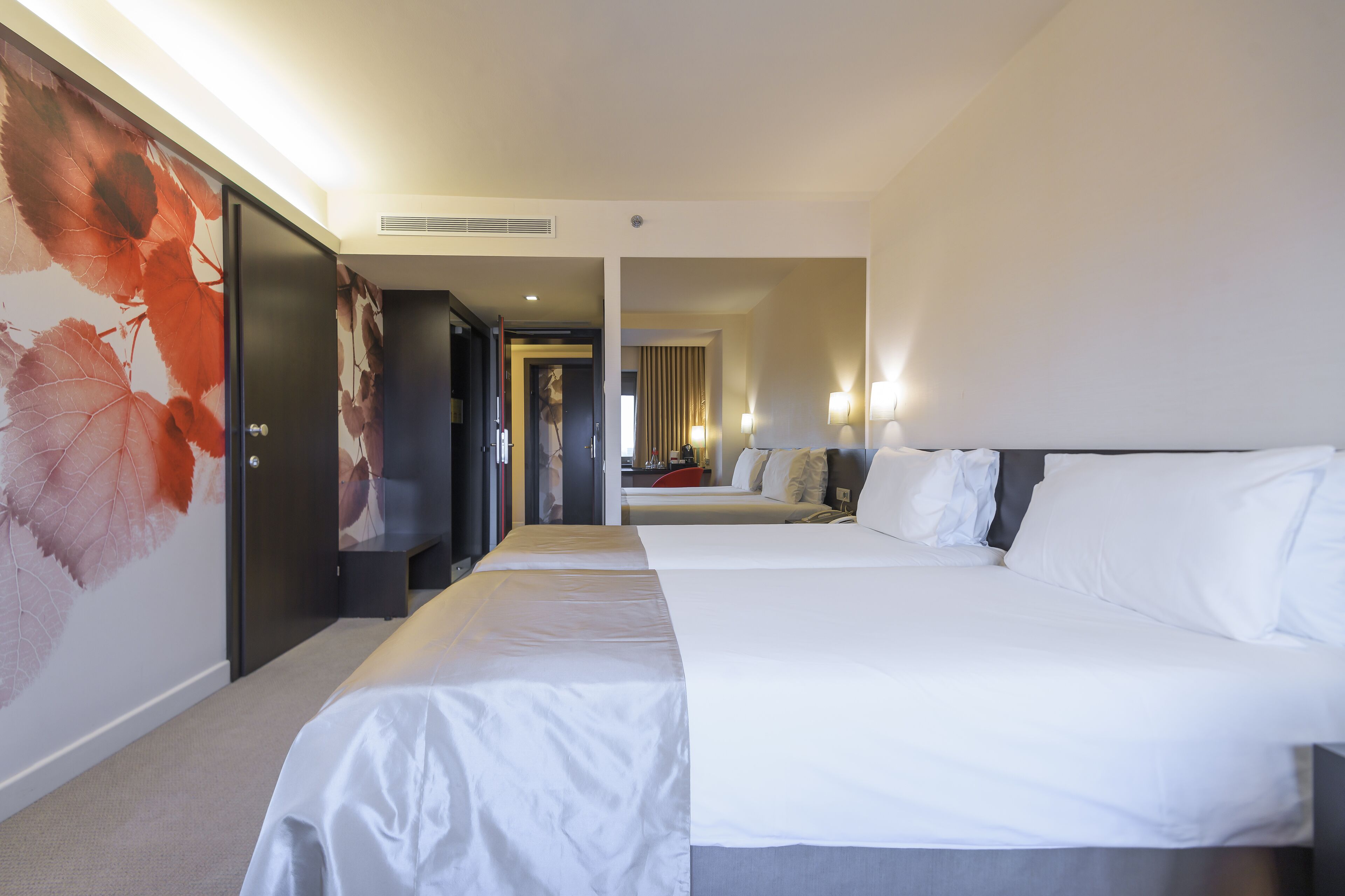 A hotel room with a large bed, a smaller bed, a wardrobe, and a wall with a leaf pattern.