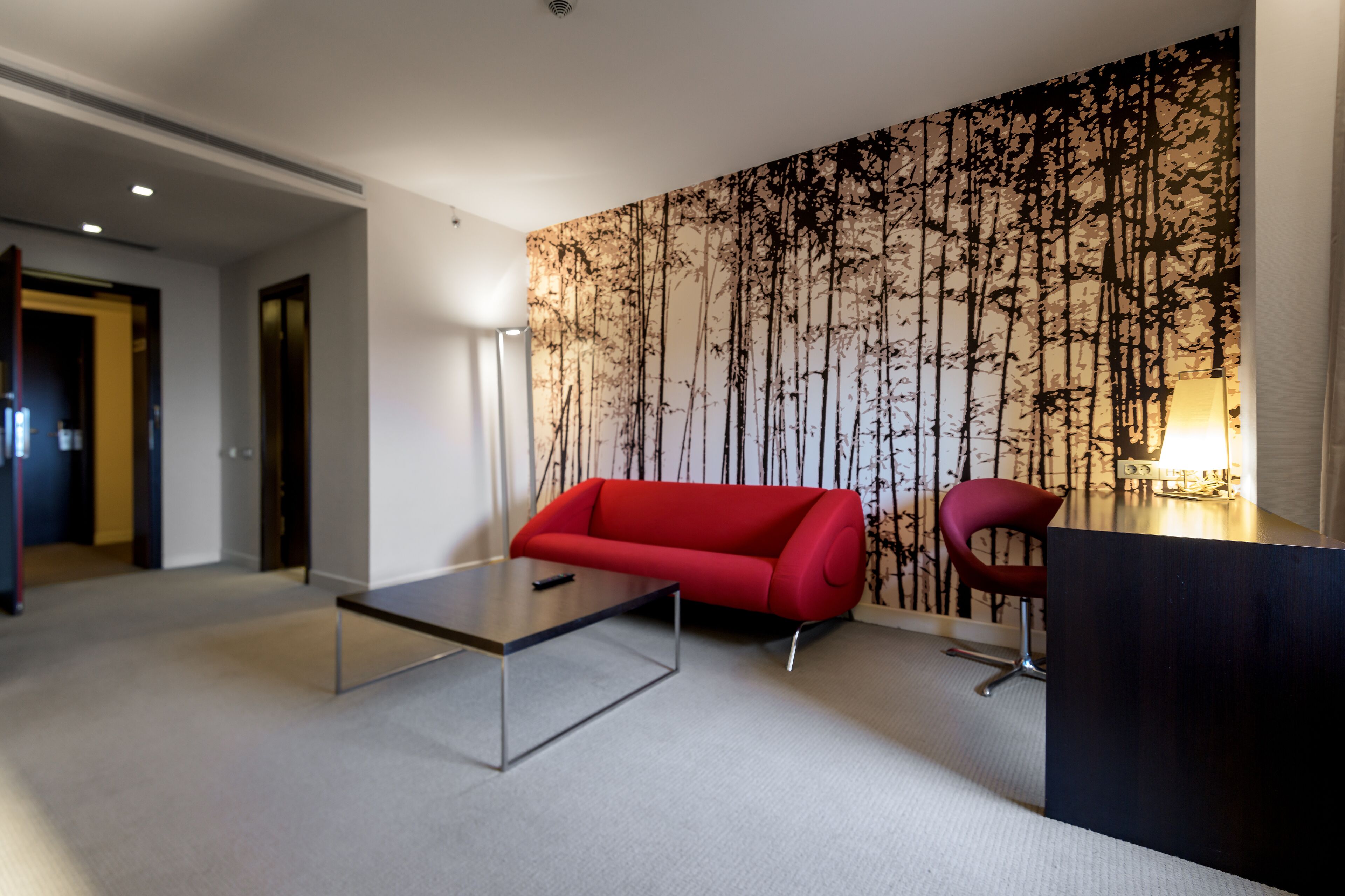 Un moderno vestíbulo de hotel con un sofá rojo, una mesa de centro de vidrio y un escritorio con una silla.