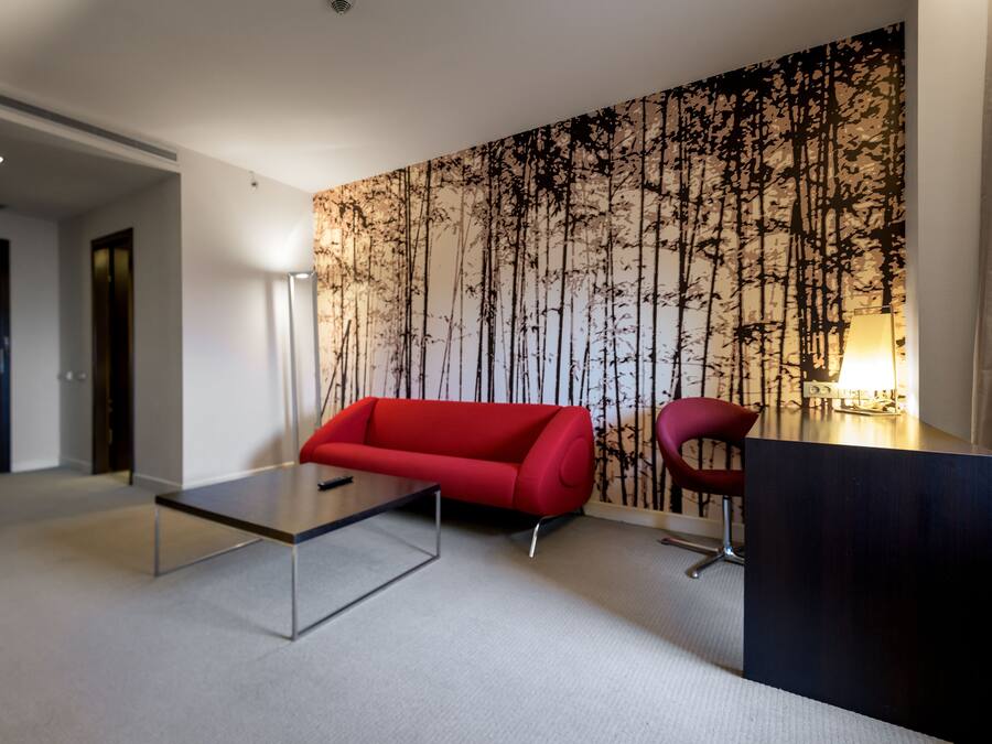 Un moderno vestíbulo de hotel con un sofá rojo, una mesa de centro de vidrio y un escritorio con una silla.