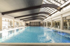 An indoor swimming pool with a modern design, featuring a large pool area, lounge chairs, and a high ceiling with skylights. - Ramada Plaza by Wyndham Bucharest Convention Center (Bucharest)