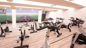 A gym with multiple stationary bikes and treadmills, a mirrored wall, and a large window with a road view.