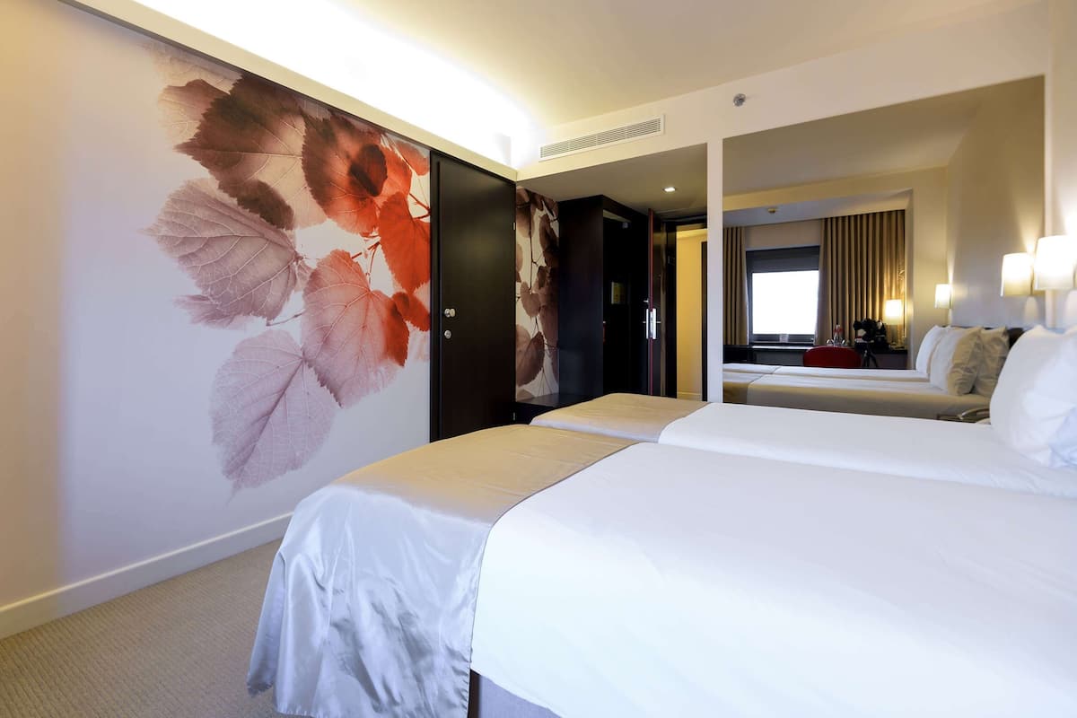 Ein Hotelzimmer mit einem großen Bett, einem Nachttisch, einem Spiegel und einer Wand mit einem Blattmuster.