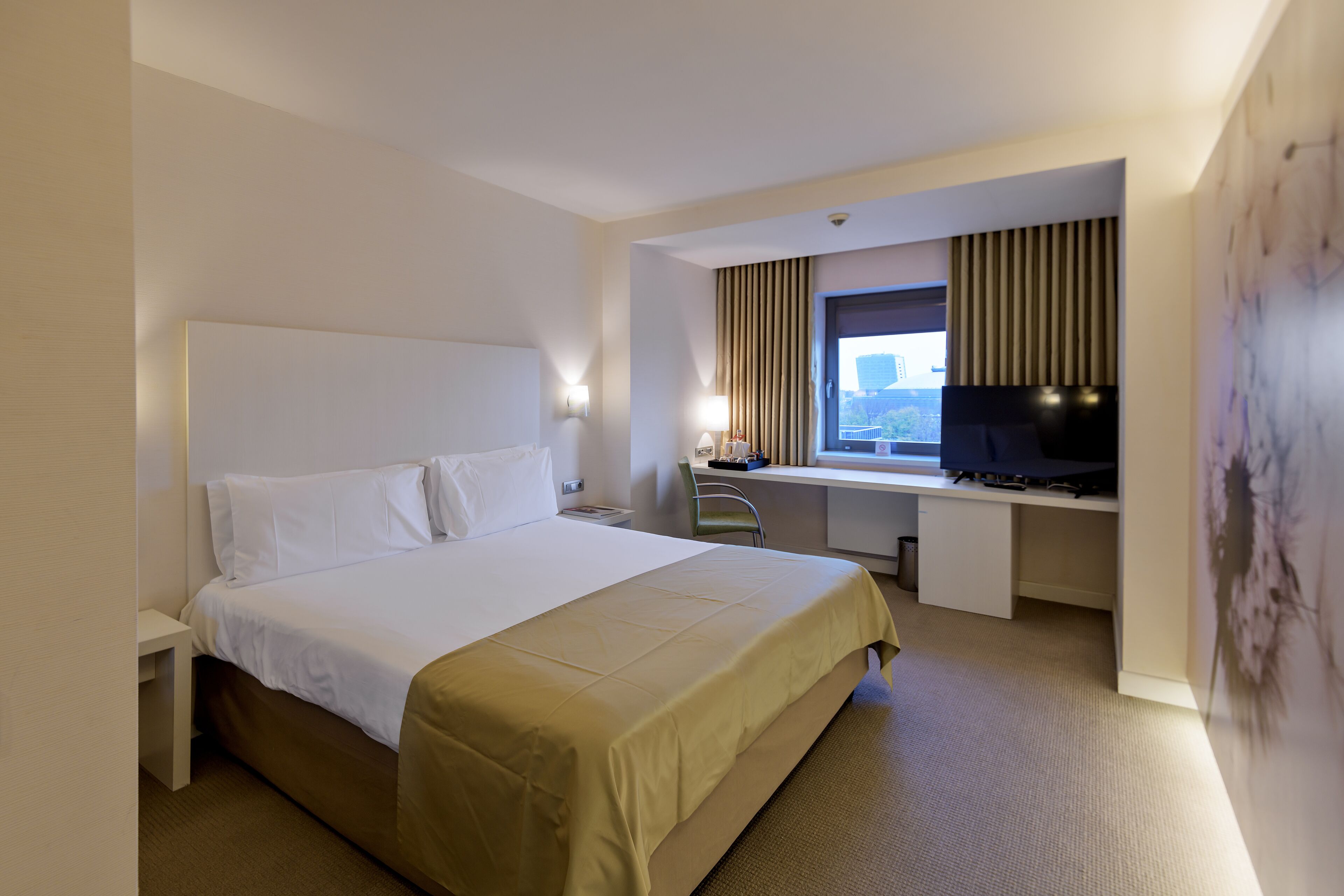 Habitación de hotel con cama, escritorio, silla y televisor.