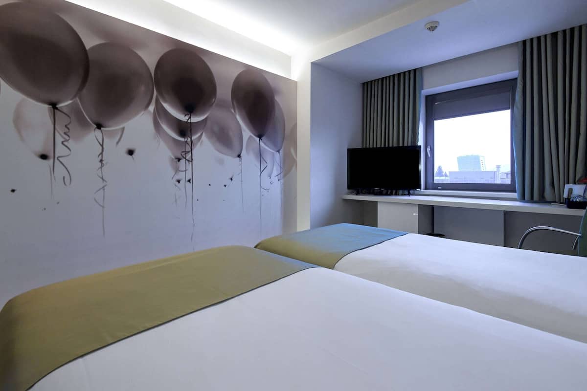 Ein Hotelzimmer mit zwei Betten, einem Flachbildfernseher, einem Fenster mit Vorhängen und einer Wand mit Ballons.