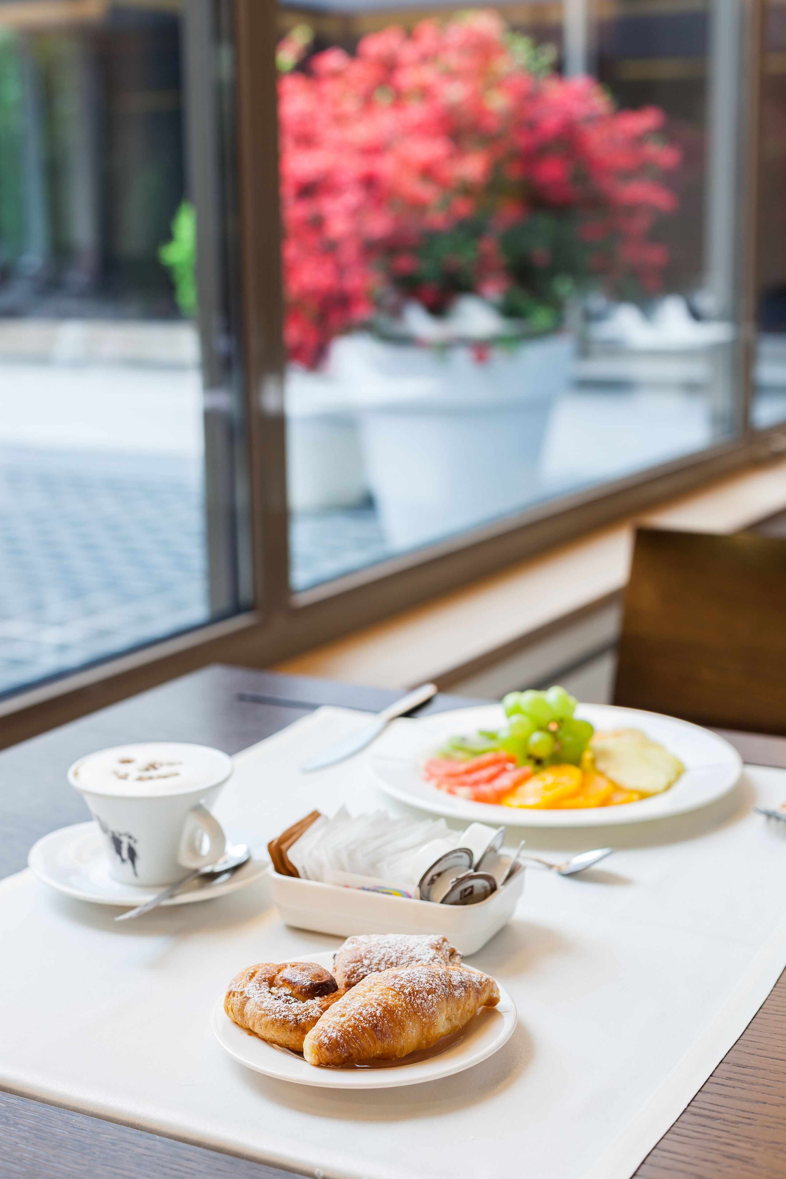 Una mesa de desayuno con pasteles, una taza de café y un plato de fruta.