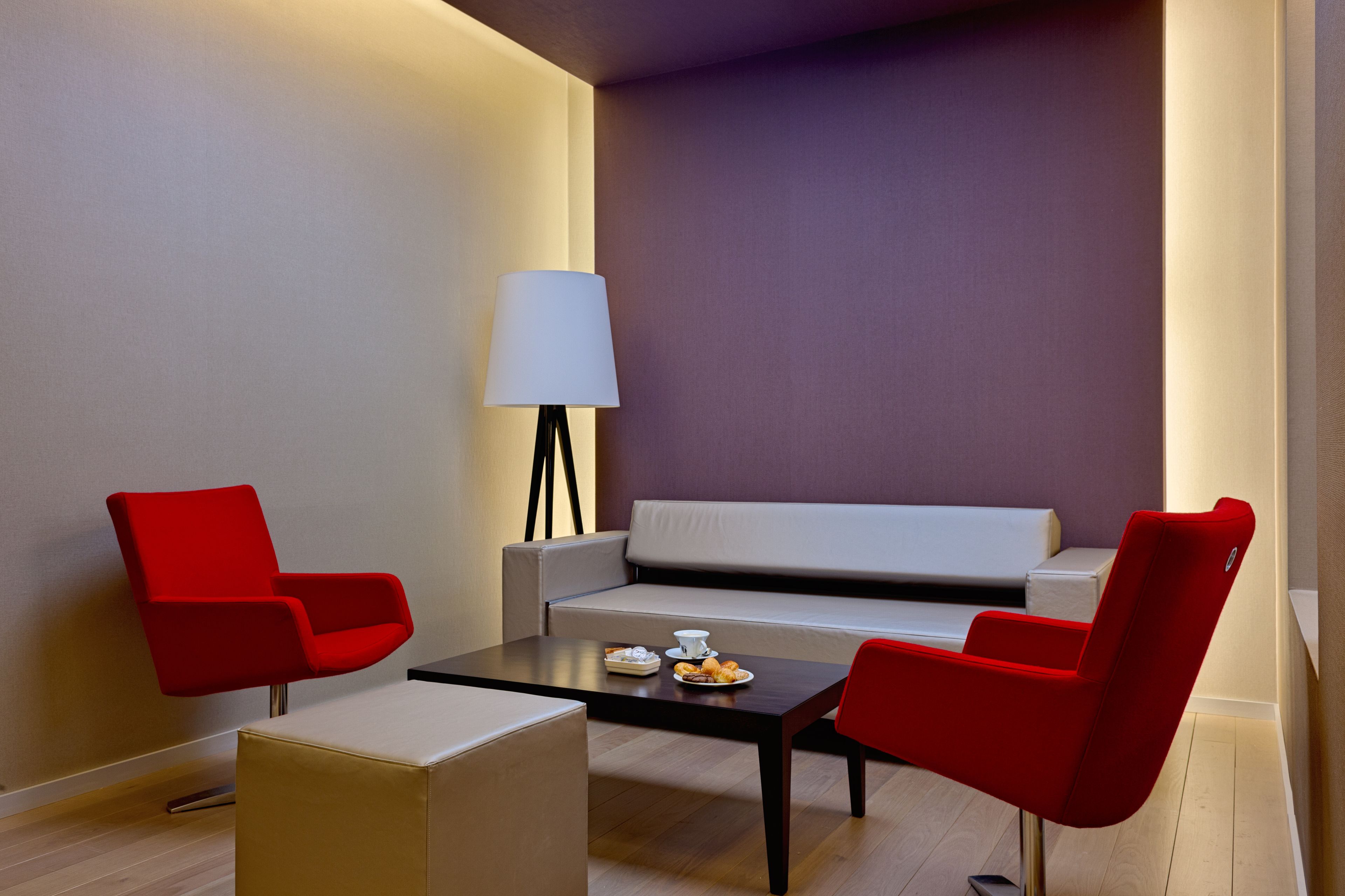Et moderne værelse med sofa, to røde stole, et sofabord og en lampe.