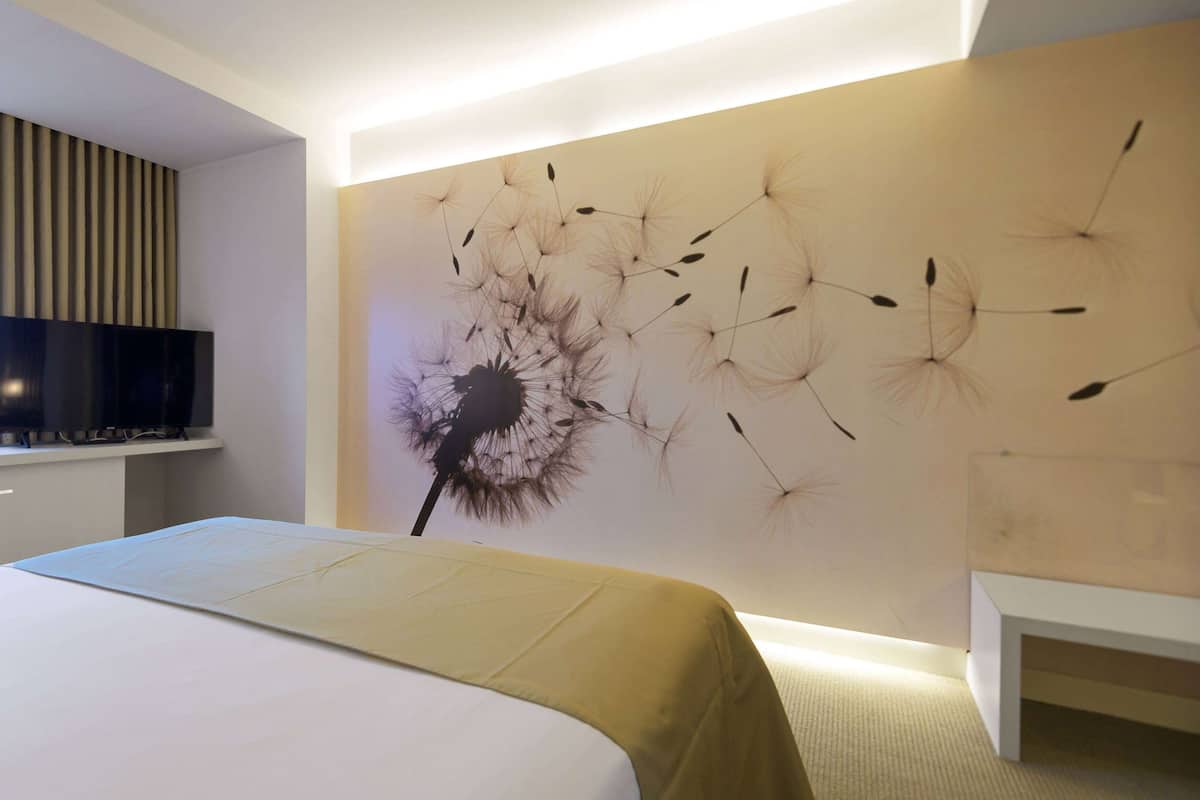 Ein modernes Schlafzimmer mit einem großen Bett, einem an der Wand montierten Fernseher und einem dekorativen Wandbild.