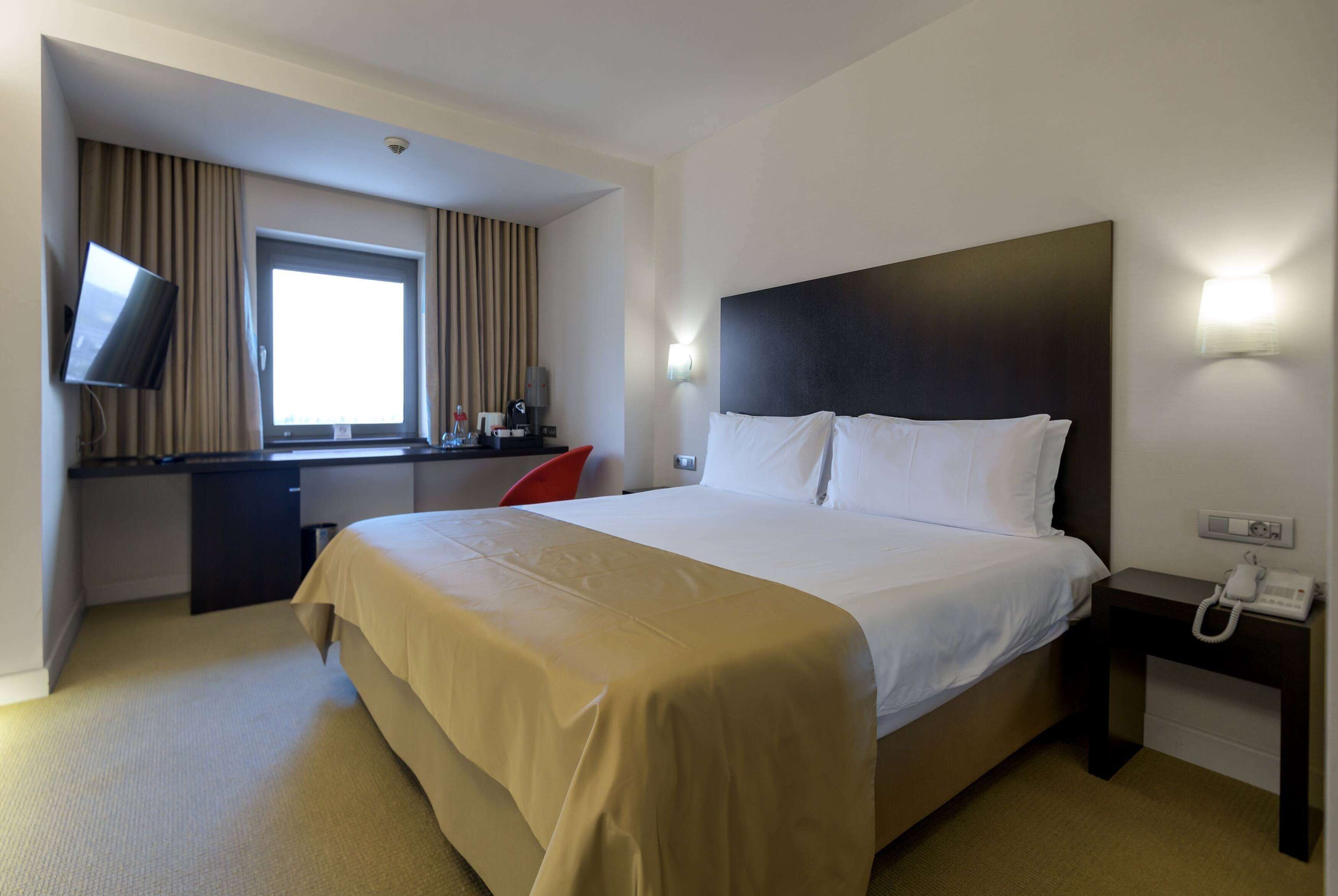 A hotel room with a bed, a desk, a television, and a telephone.