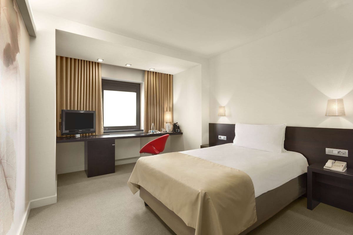 Ein Hotelzimmer mit Bett, Schreibtisch, Fernseher und zwei Nachttischlampen.