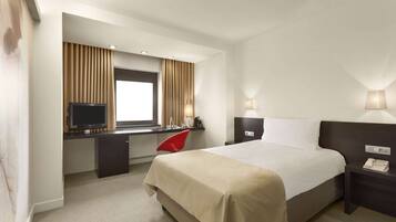 Habitación de hotel con cama, escritorio, televisión y dos lámparas de noche.