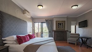 A hotel room with a large bed, a fireplace, a TV, and a balcony with a view. - Greenway Woods Resort (Mbombela)
