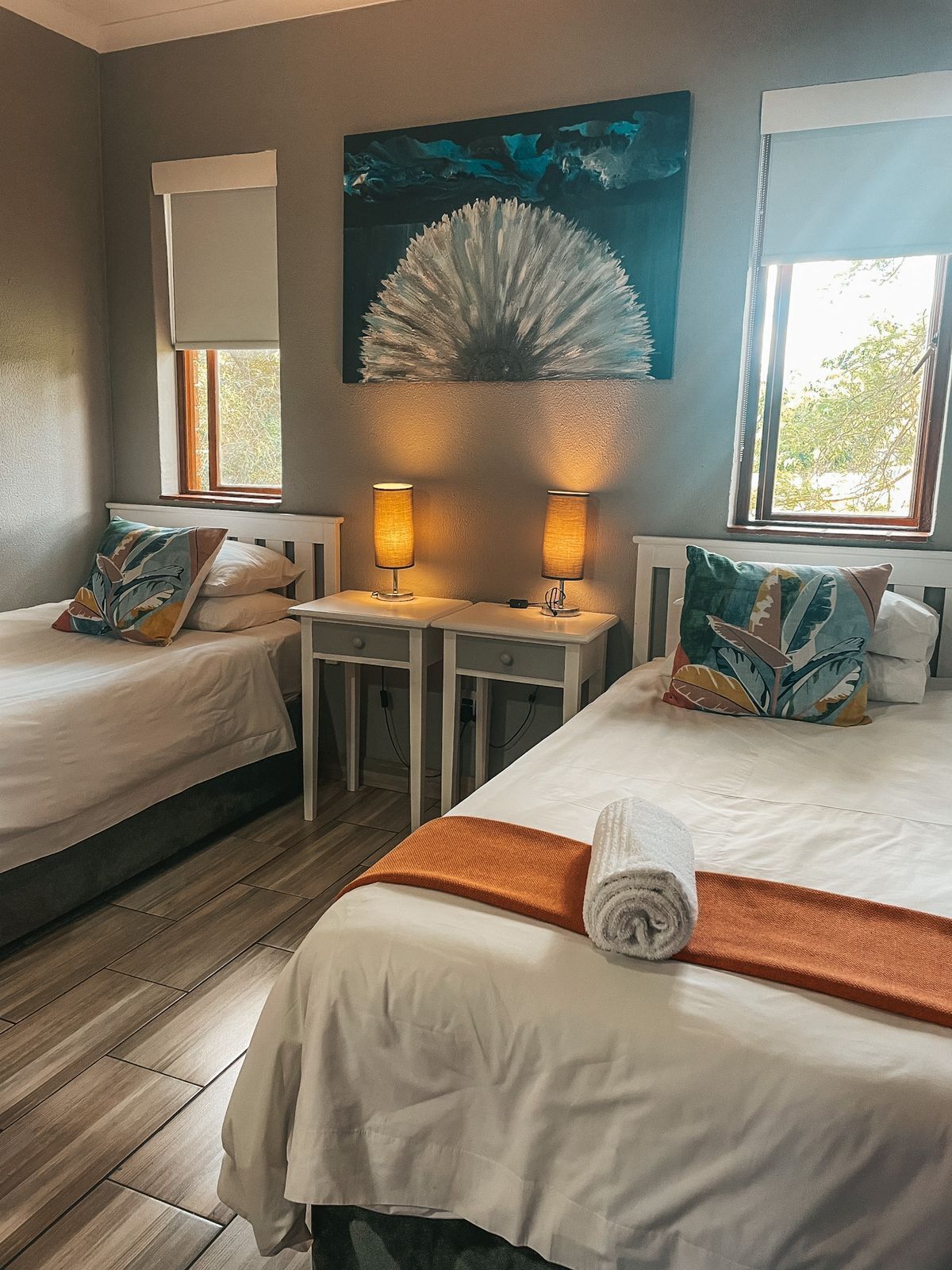 Habitación de hotel con dos camas, un cuadro, una ventana y una mesa con lámparas.