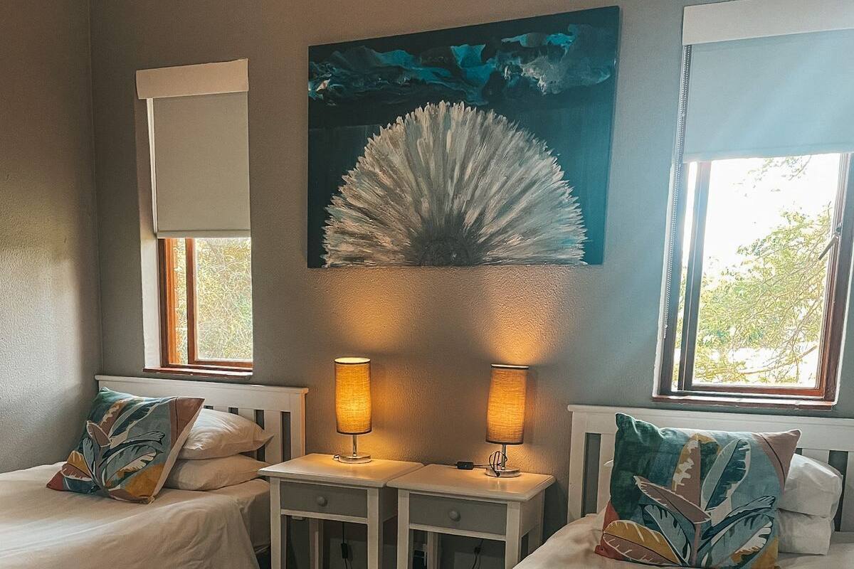 Habitación de hotel con dos camas, un cuadro, una ventana y una mesa con lámparas.