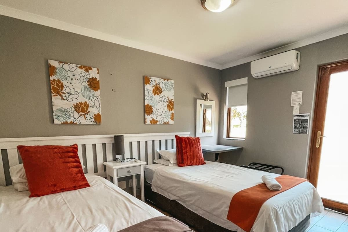 A hotel room with two beds, a desk, a mirror, and an air conditioning unit.
