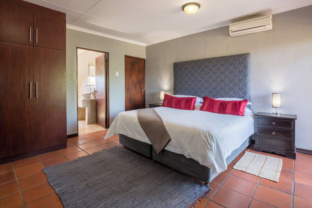 A bedroom with a bed, nightstands, a wardrobe, and an air conditioning unit.