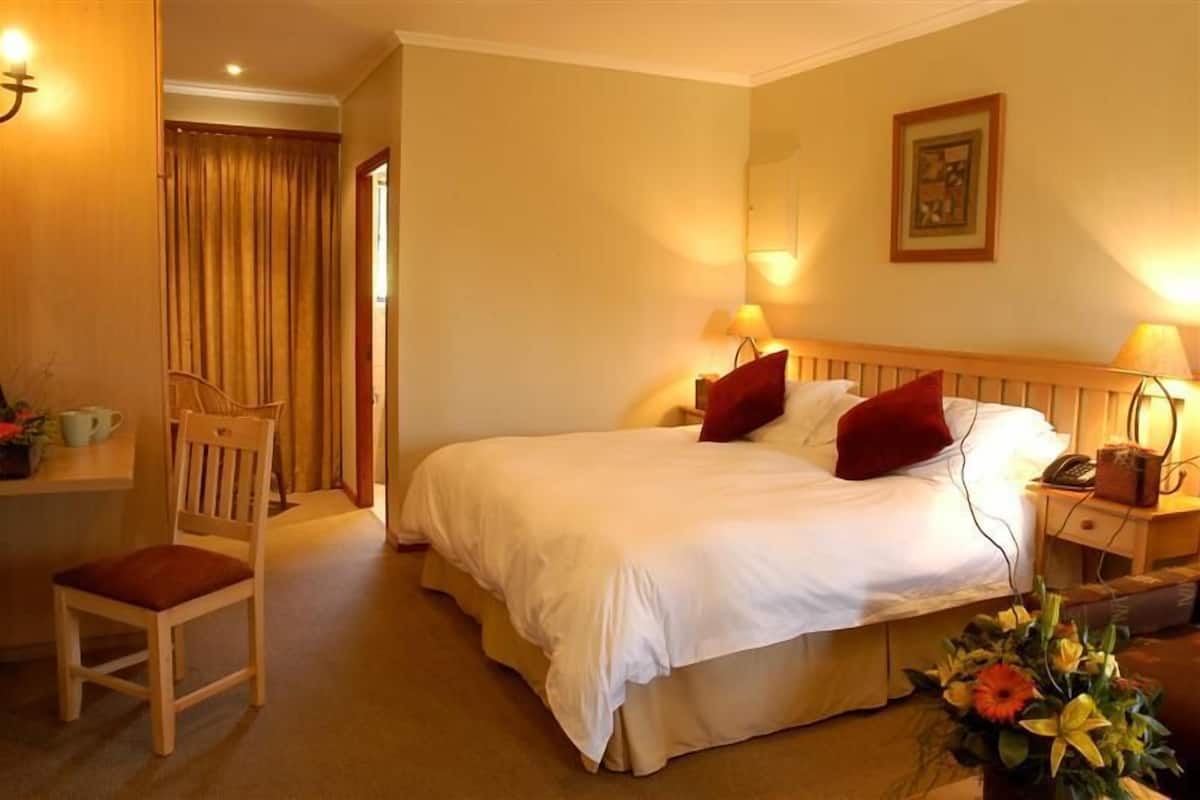 A hotel room with a bed, bedside lamps, a chair, a desk, and a mirror.
