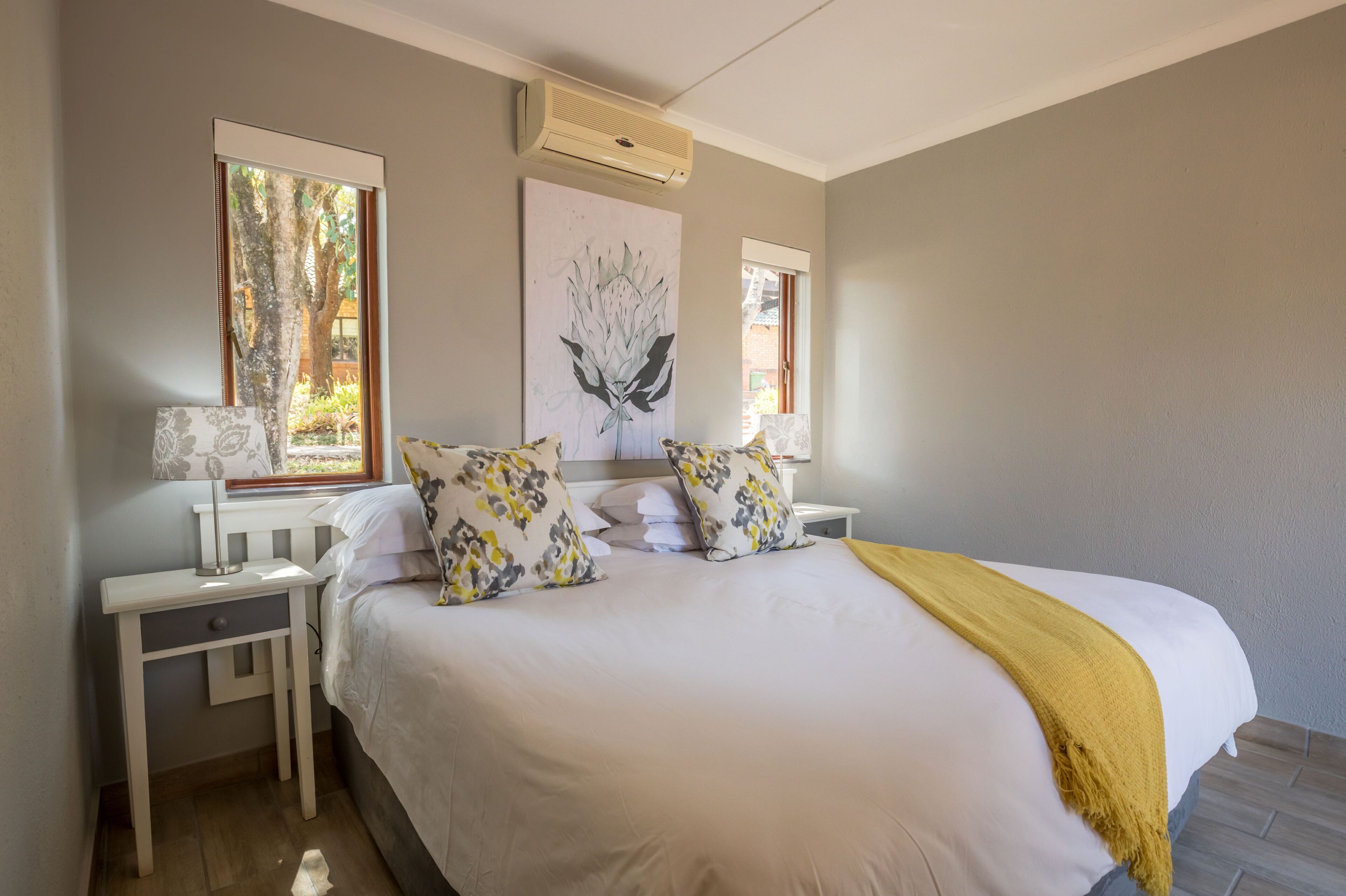 A bedroom with a large bed, two nightstands, a window with a view, and an air conditioning unit.