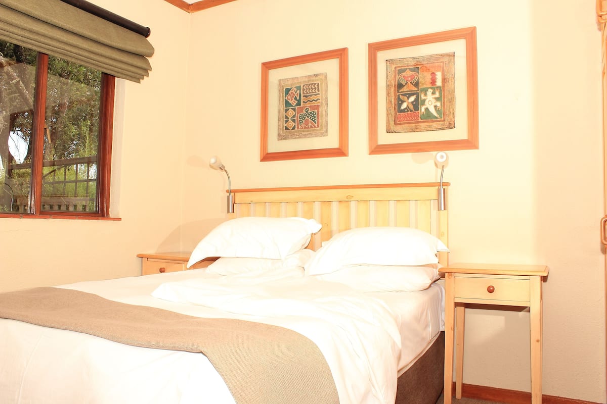 A neatly made bed with white linens, a wooden headboard, and two framed artworks on the wall.