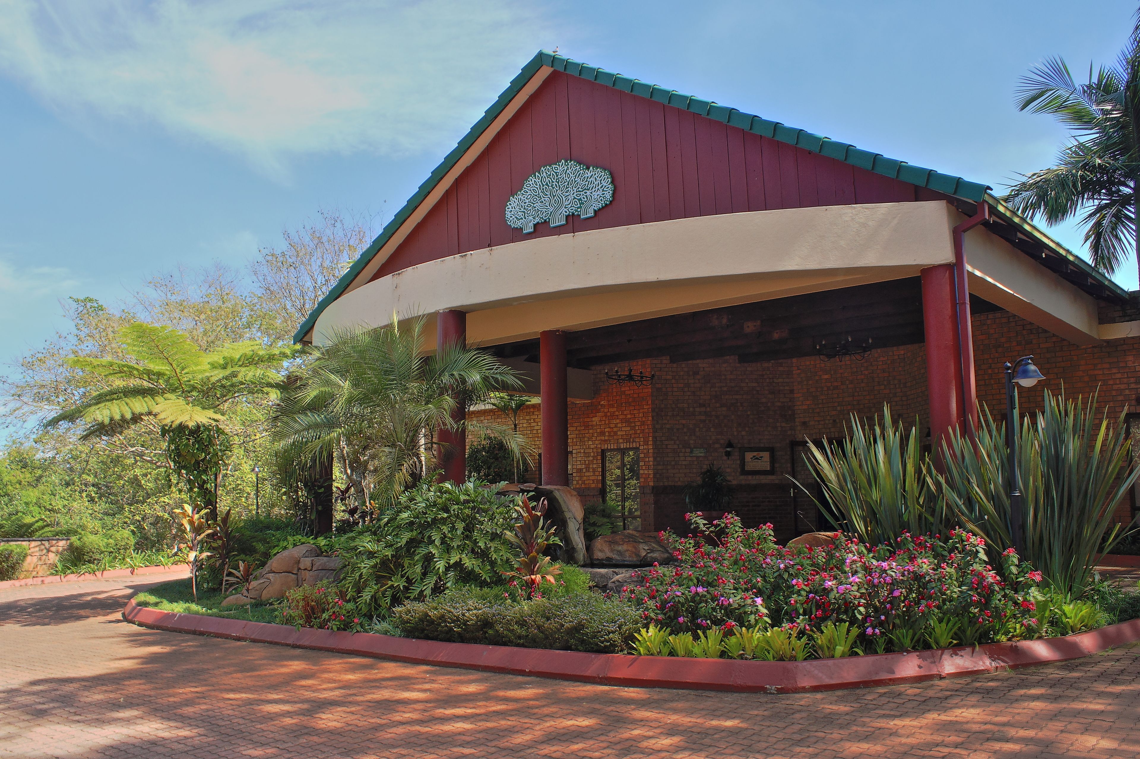 A building with a curved roof, a large tree logo on the facade, and a landscaped garden with various plants and flowers.