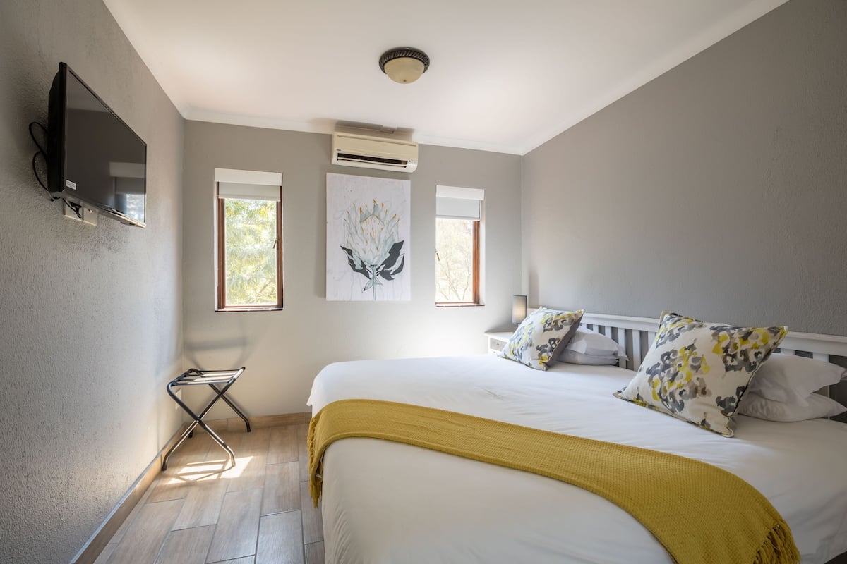 A bedroom with a bed, a TV mounted on the wall, and a window.