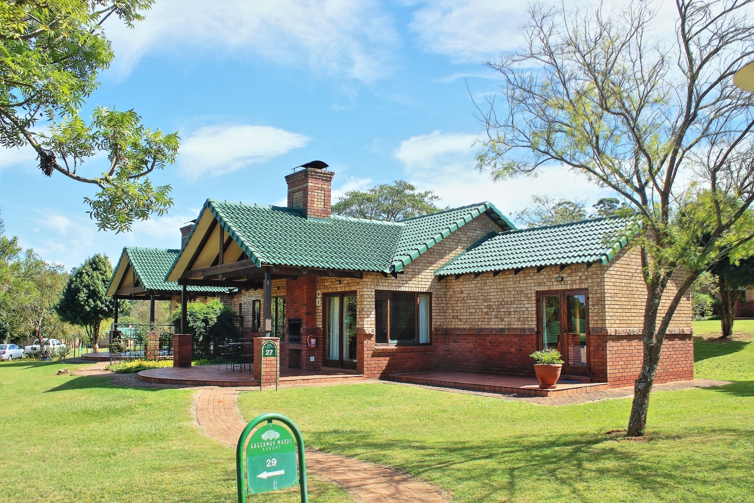 A brick building with a green roof, a covered patio, and a sign indicating room number 27.