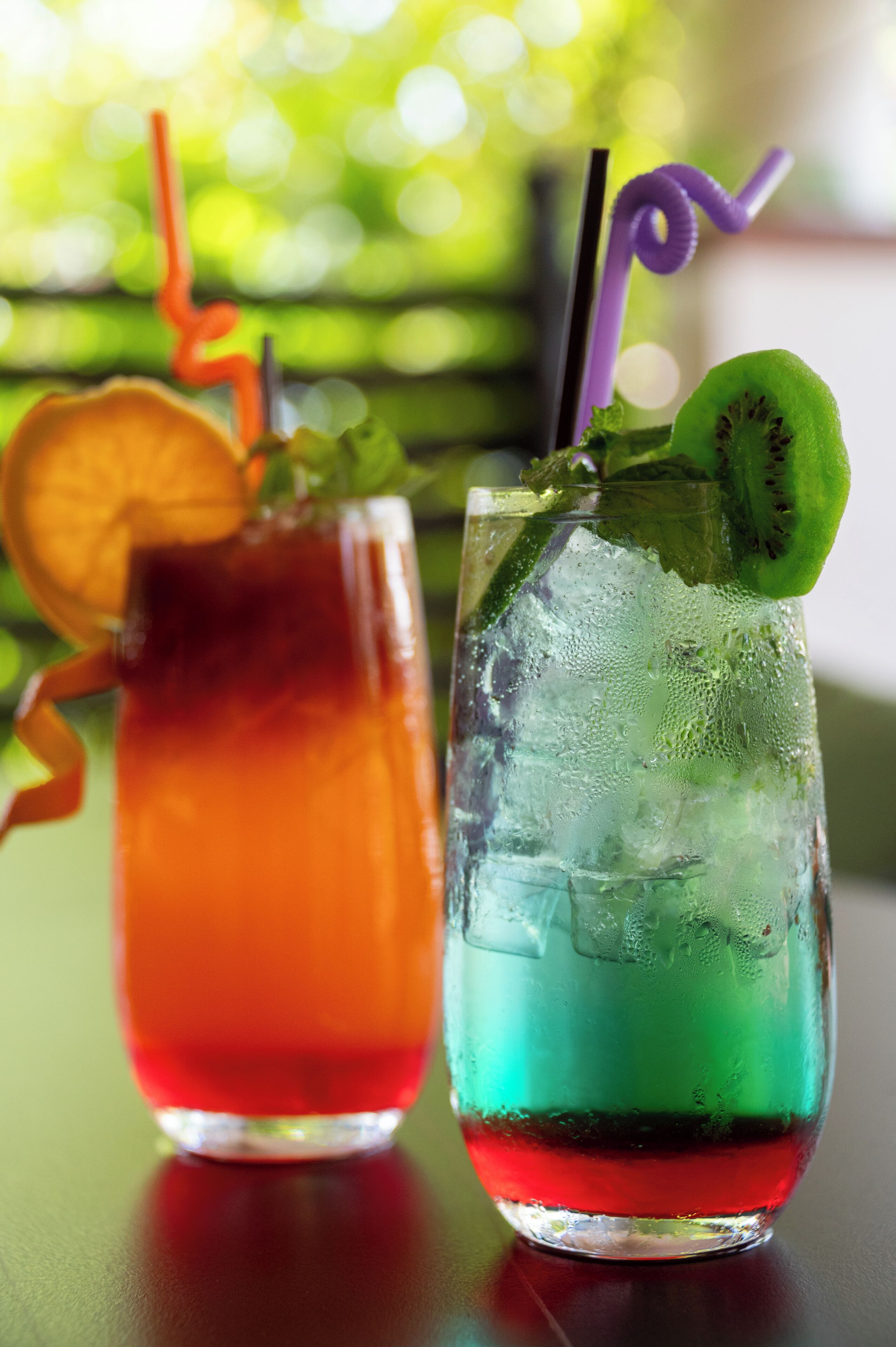 Two cocktails with straws and garnishes on a table.