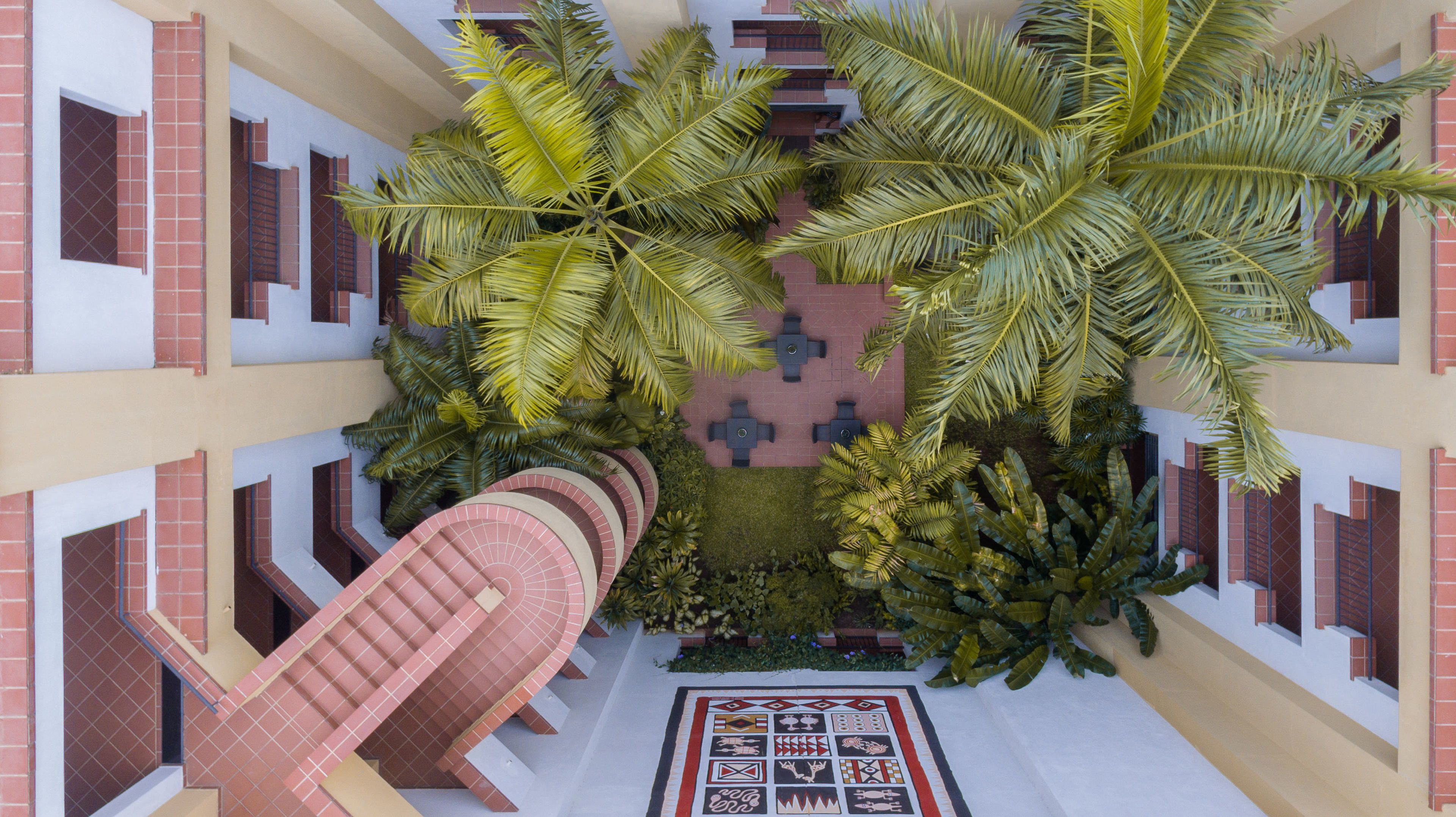 Un atrio de varios niveles con un patio central, que cuenta con una escalera en espiral, asientos al aire libre y exuberantes plantas tropicales.