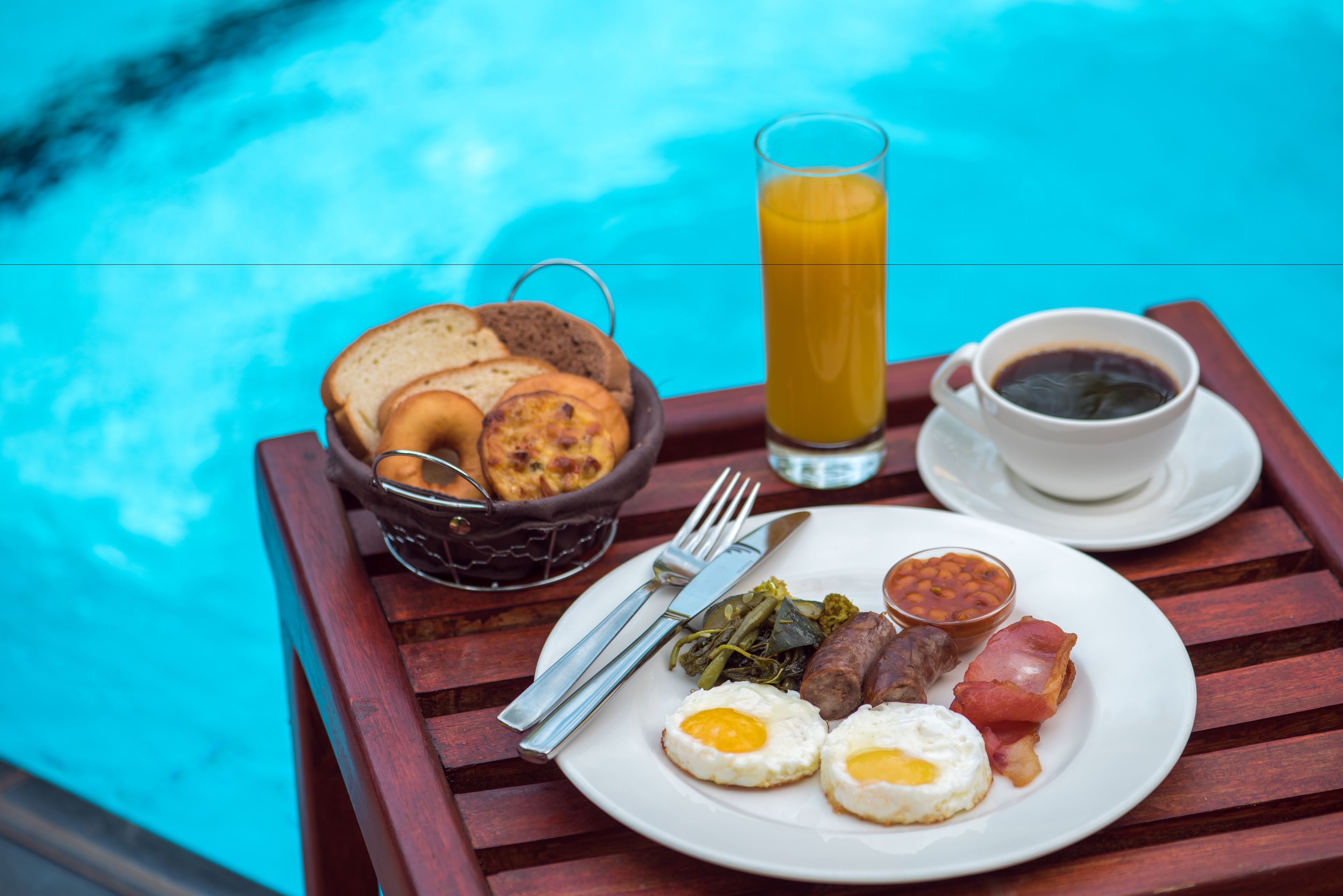 Bandeja de desayuno con huevos, tocino, frijoles y tostadas junto a una piscina.