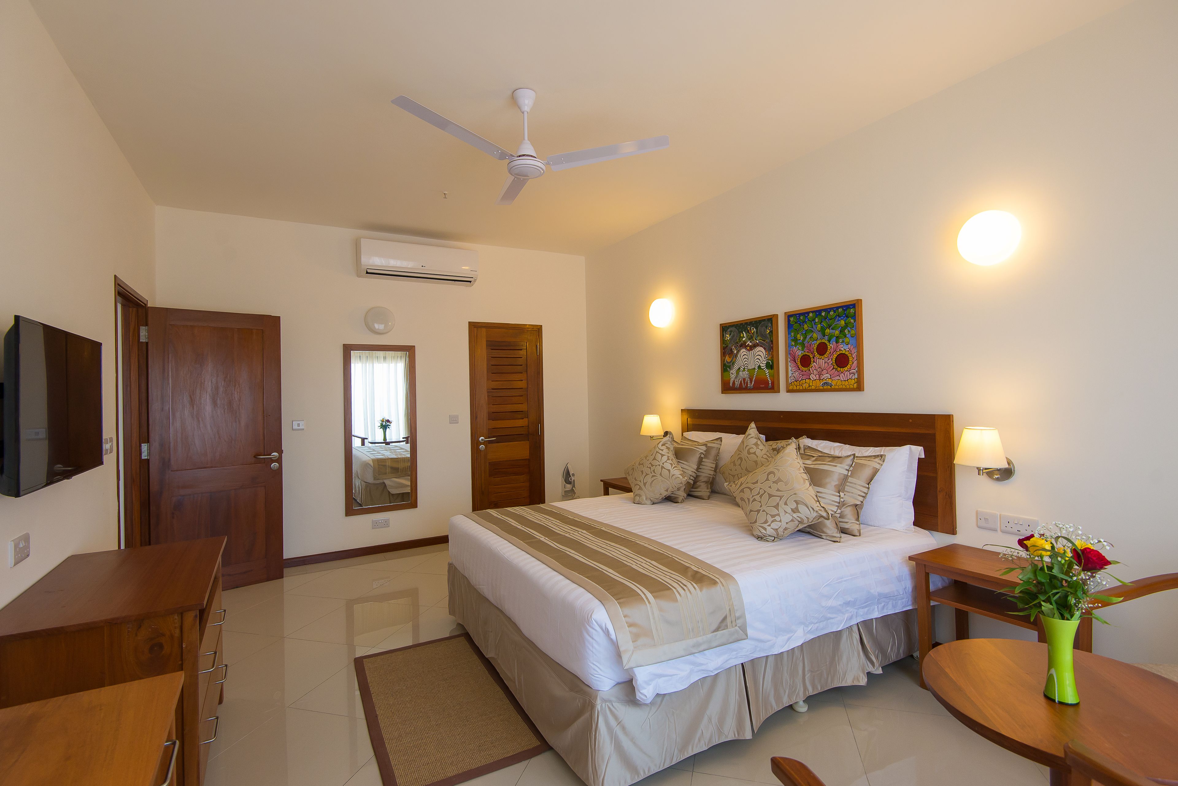 Una habitación de hotel con cama, mesitas de noche, escritorio, silla, ventilador de techo y televisor montado en la pared.