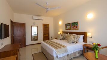 A hotel room with a bed, bedside tables, a desk, a chair, a ceiling fan, and a wall-mounted TV.