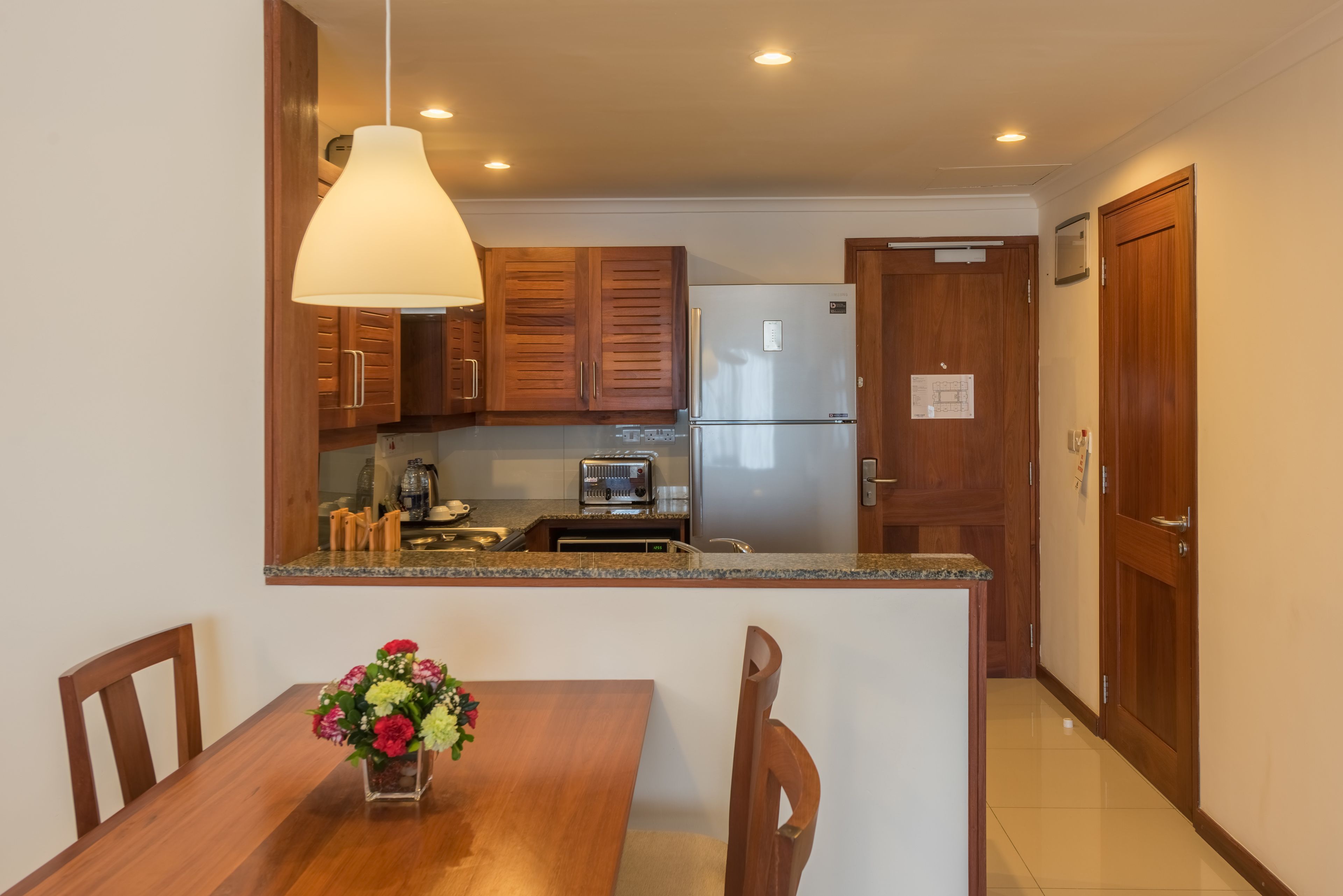 A compact kitchen with wooden cabinets, a stainless steel refrigerator, a built-in toaster, and a dining area with a wooden table and chairs.