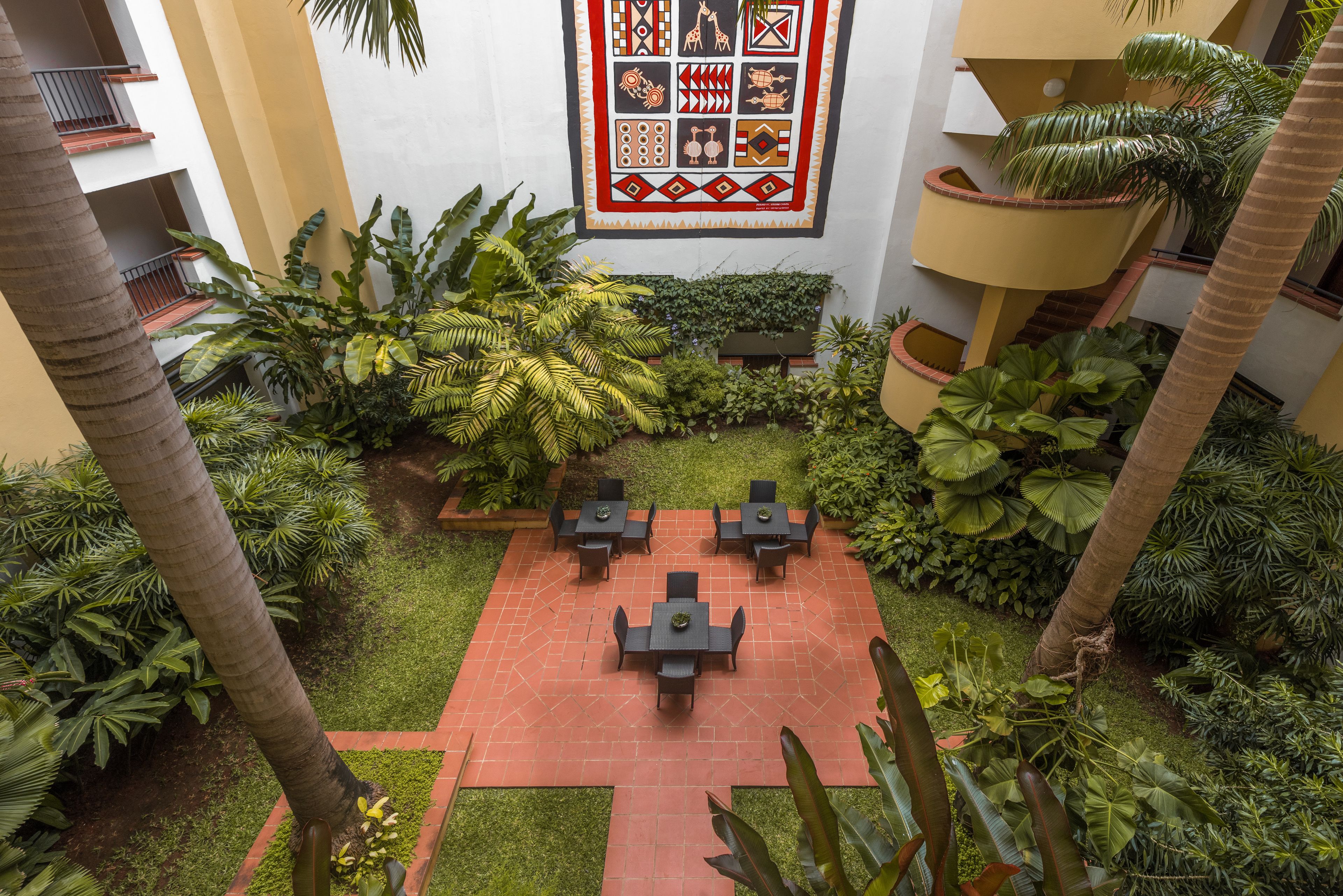 A courtyard with a central seating area, surrounded by lush greenery and a decorative wall.