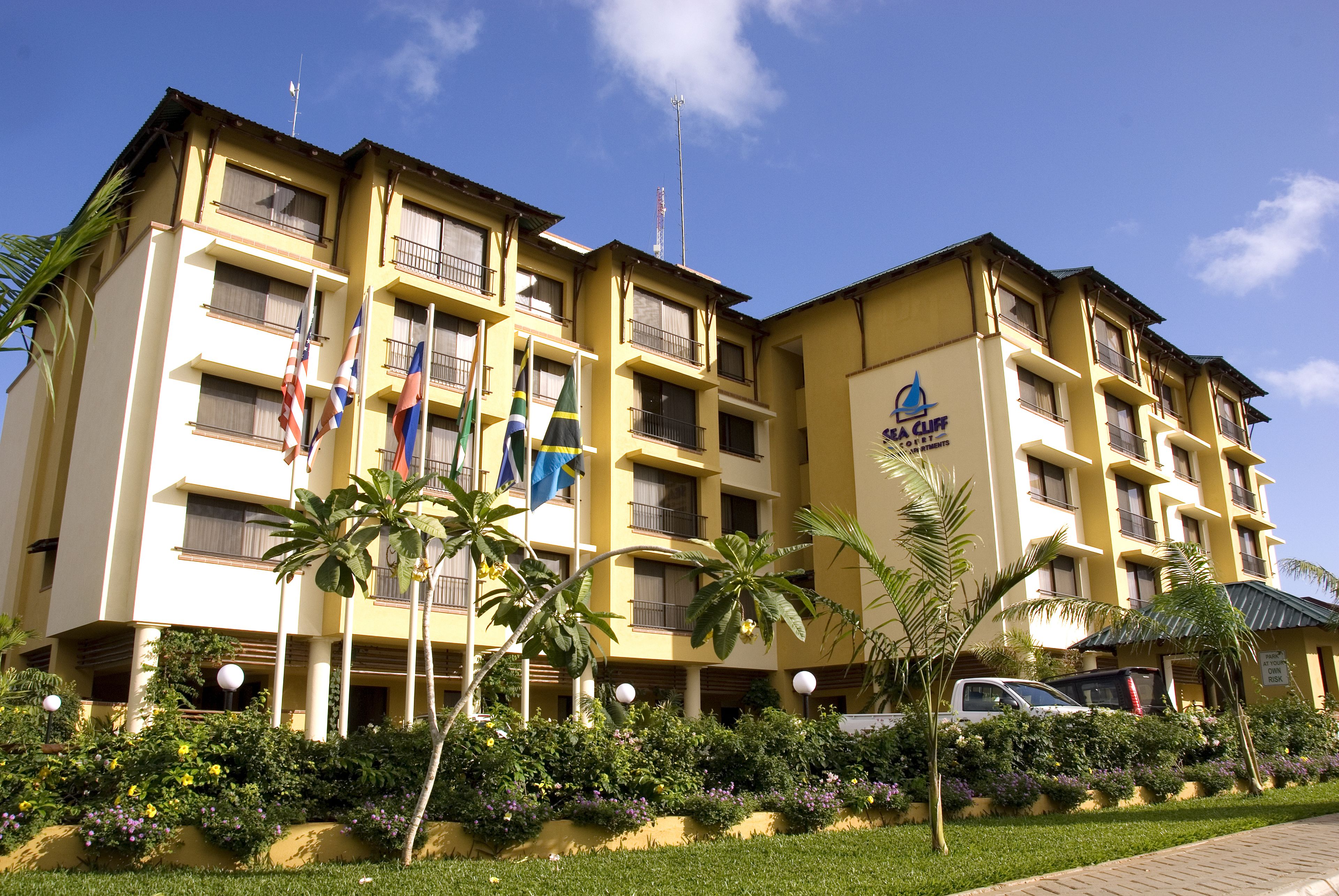 A multi-story hotel with balconies, a sign indicating it is a hotel, and flags.