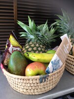 A woven basket containing a pineapple, a banana, a mango, an apple, and a package of snacks.