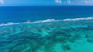 An aerial view of a coastal area with clear turquoise waters and a boat in the distance. - Sunbreeze Suites (San Pedro)