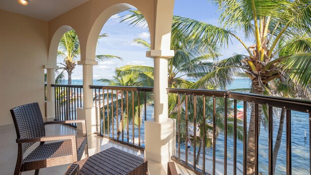 A balcony with wicker furniture, a view of the ocean, and palm trees. - Sunbreeze Suites (San Pedro)