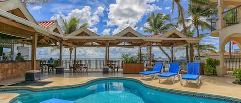 A pool area with lounge chairs and a view of the ocean.