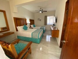 Habitación de hotel con dos camas, un escritorio, una silla, un ventilador de techo y un espejo grande.