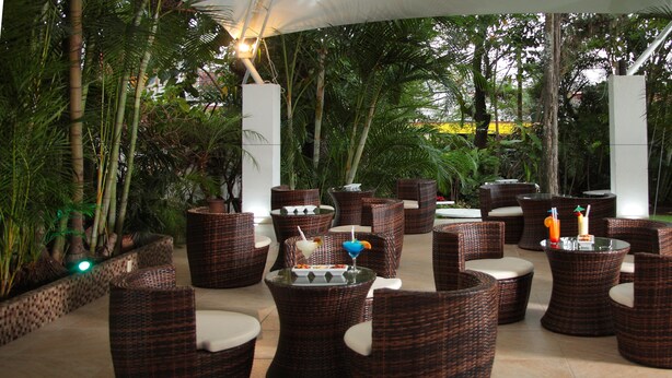 An outdoor seating area with wicker furniture and glass tables, surrounded by lush greenery. - Hotel Quinta Las Flores (Cuernavaca)
