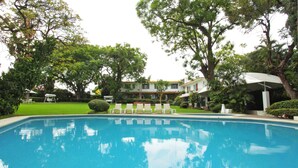 A swimming pool with lounge chairs, surrounded by trees and a building with a white facade. - Hotel Quinta Las Flores (Cuernavaca)