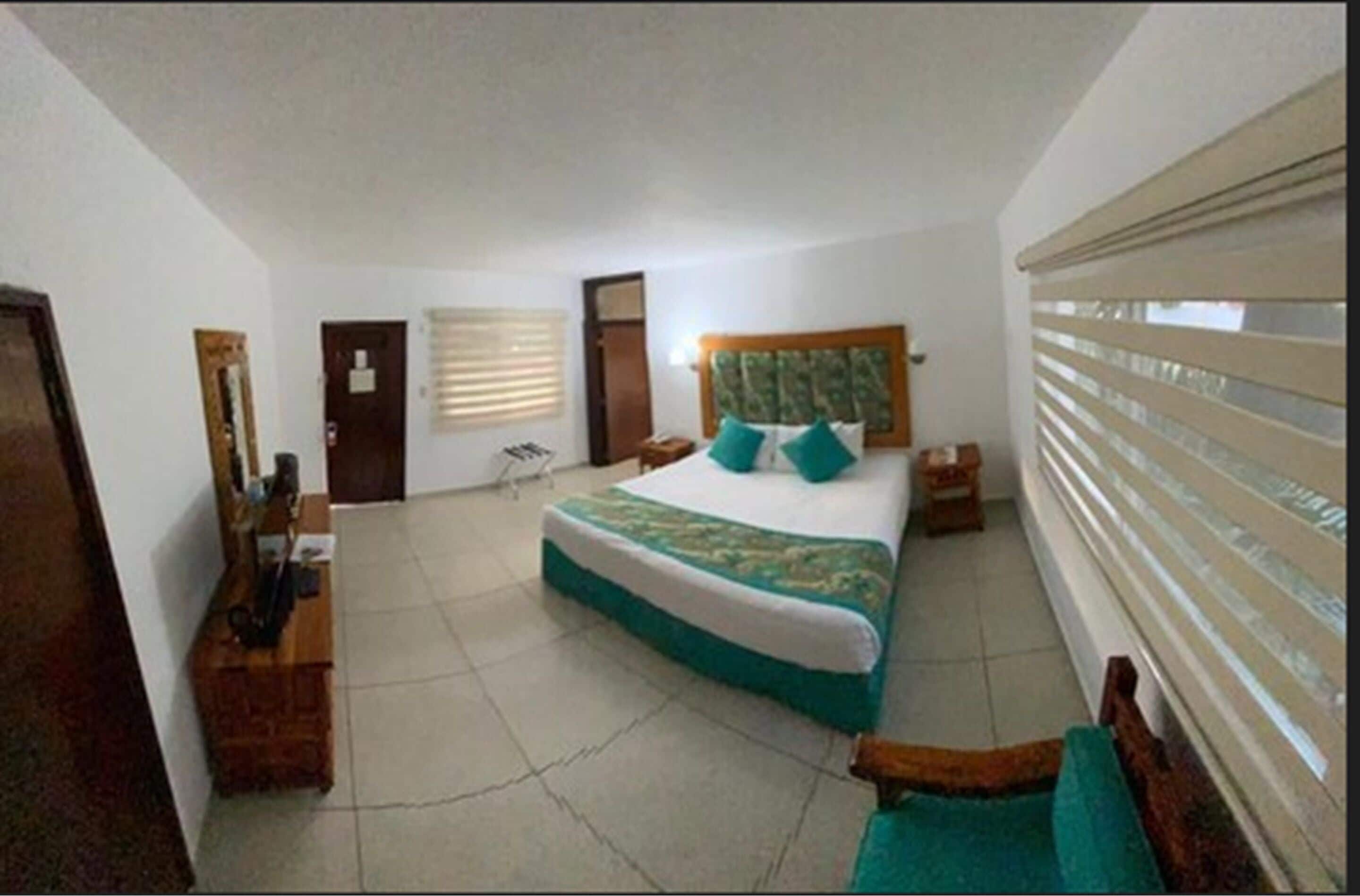 Un dormitorio con cama, mesitas de noche, un espejo, una puerta y una ventana con persianas.