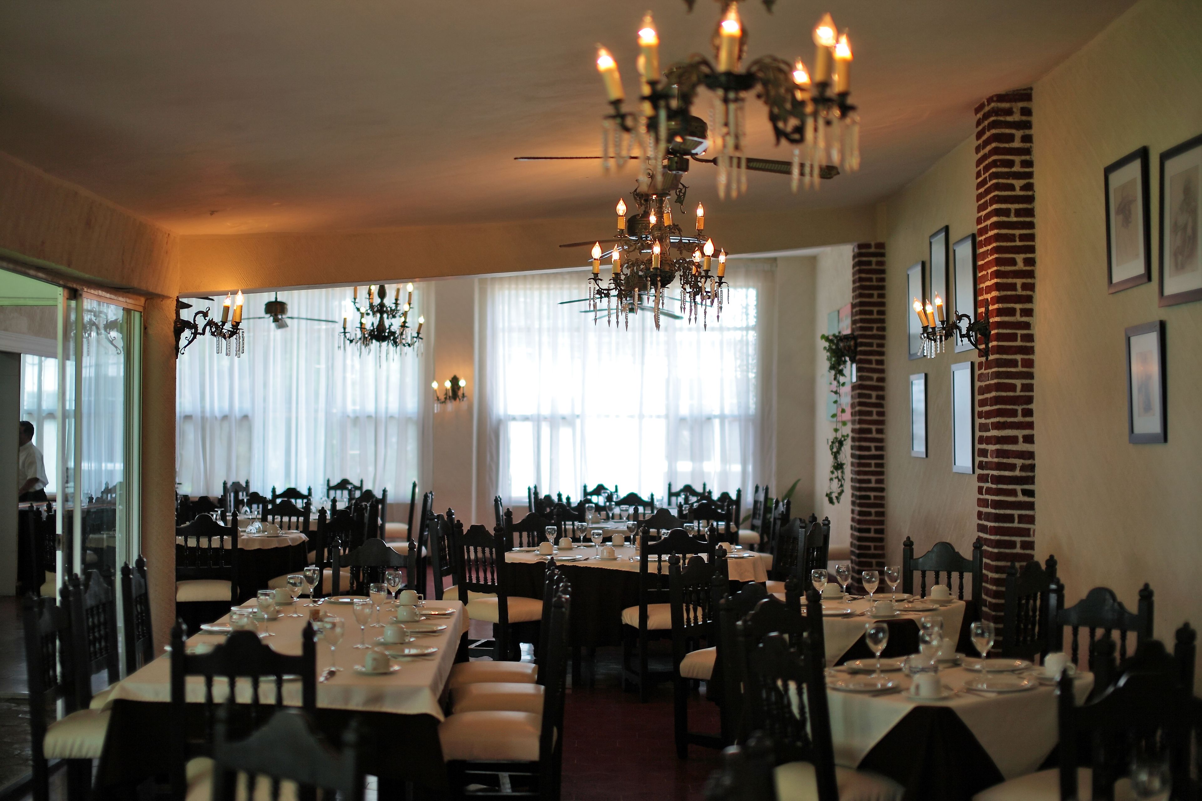 Un restaurante con varias mesas dispuestas para comer, candelabros y columnas de ladrillo.